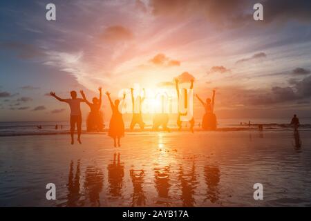 Gruppe glücklicher Freunde, die gegen Sonnenuntergang am Strand springen Stockfoto