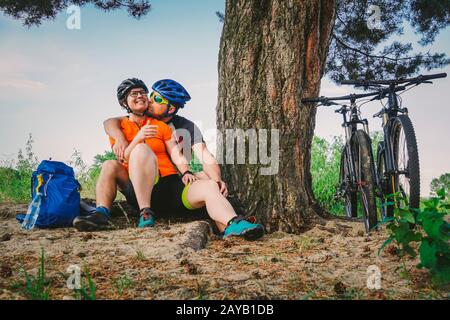 Ein glückliches Paar mit dem Mountainbike-Sit, das die Natur in der Natur umarmt, ein glückliches Paar, ein aktives Lebensgefühl, das im Wald angehalten wurde Stockfoto