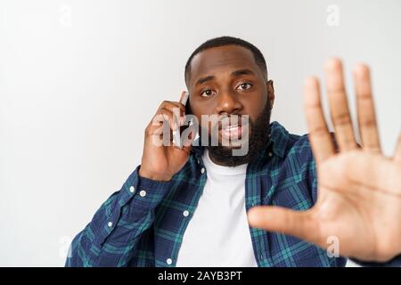 Ein junger afroamerikanischer Mann, der auf seinem Handy mit einem besorgten oder ernsthaften Blick auf sein Gesicht spricht Stockfoto