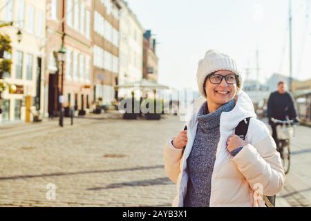 Portrait einer jungen kaukasischen europäischen Frau Touristin in Brille für den Blick auf einen weißen Hut und eine Daunenjacke mit schwarzem Rücken Stockfoto