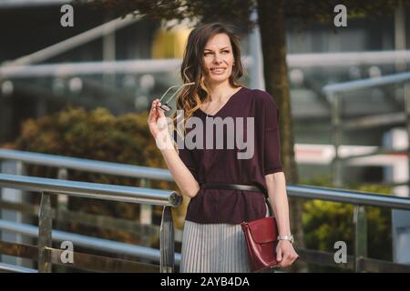 Kaukasische Erwachsene Frau in Brille in der Nähe des Bürogebäudes draußen. Business Lady im Rock hält Handbrille für die Vision Stockfoto