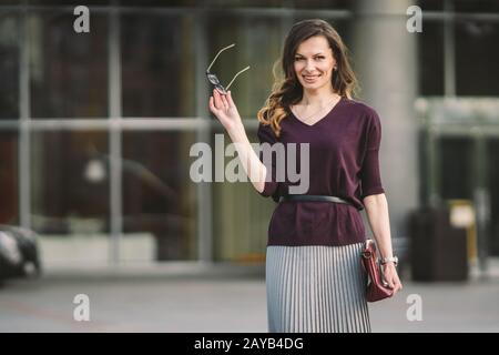 Geschäftsfrau steht auf Straße gegen Bürogebäude. Frau aus der Stadt, die arbeitet. Portrait Business Woman lächelt mit gla Stockfoto