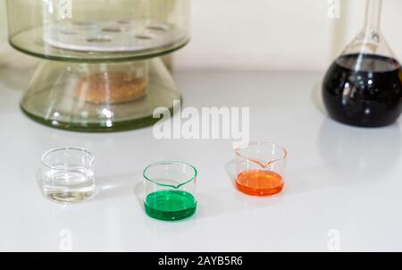 Bunte Lösungen für chemische Flüssigkeiten in Glaskolben auf weißem Laborarbeitsplatt Stockfoto