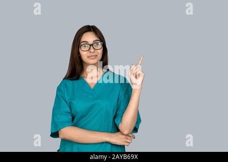 Lächelnde junge indische Krankenschwester zeigen auf den Kopierraum auf grauem Hintergrund Stockfoto
