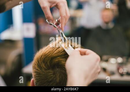 Barber Macht Haarschnitt Bearded Man In Barbershop. Professioneller Stylist, der die Haare von Kunden im Salon schneidet. Barber mit Schere und Co Stockfoto
