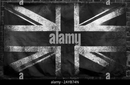 Monochromes Bild einer alten schmutzigen union Jack britische Flagge mit dunklen zerknitterten Kanten auf einem Backstein-Wand-Hintergrund Stockfoto