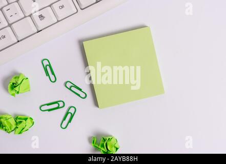 Quadratisches leeres grünes Notizpapier mit Bleistift auf weißem Hintergrund und pc-Tastatur. Flaches Lay über leerem Notizpapier für Textundurcheinander Stockfoto