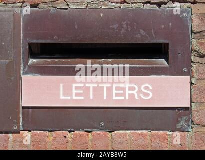 Alter britischer Postkasten in einer Ziegelwand mit verrosteter Metallumfassung und den Wortbuchstaben auf einer verblassten roten Tafel Stockfoto