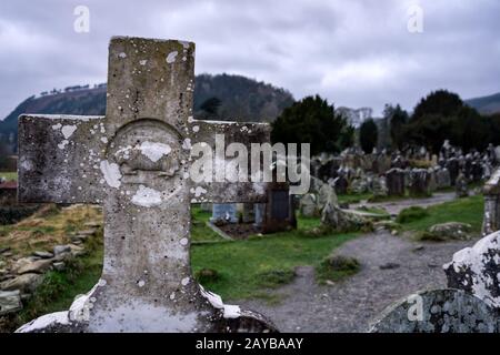 Alt-katholische Kreuz aus Granit auf Grabstein mit Friedhof und Grabsteinen im Hintergrund, Glendalough, Ire Stockfoto