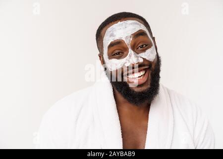 Junger afroamerikanischer Kerl, der Gesichtscreme auf weißem Hintergrund anwendet. Portrait eines jungen fröhlichen, lächelnden afrikaners im Studio. Hig Stockfoto