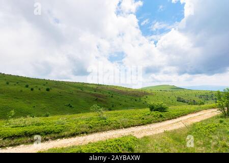 Mountain dirt road Landschaft. Pfad durch die grünen Wiesen auf sanften Hügeln. ridge in der Ferne. grüne Landschaft der Karpaten. bewölkt Sommer Wetter Stockfoto