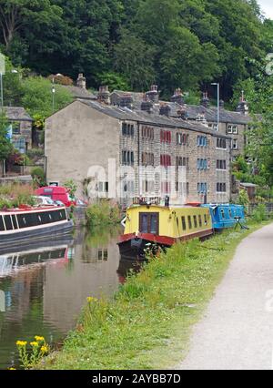 Der rochdale Kanal, der durch die hebdenbrücke mit vermauerten Booten verläuft, spiegelte sich in den von Bäumen umgebenen Wasser- und Steingebäuden wider Stockfoto