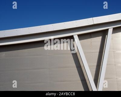 Metallische Verkleidung am modernen Industriegebäude mit Stahlträgern und gebogenem Dachträger gegen einen blauen Himmel Stockfoto