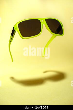 Grün schwimmend in der Luftsonnenbrille auf gelbem Hintergrund. Stockfoto