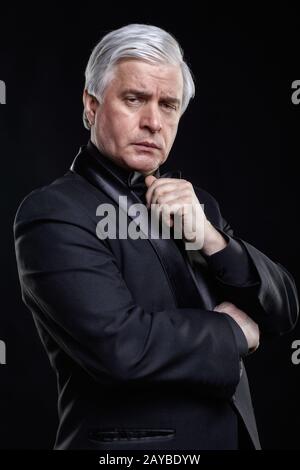 Reifer Mann in schwarzem Anzug, der die Kamera mit hypnotischem Look betrachtet. Stockfoto