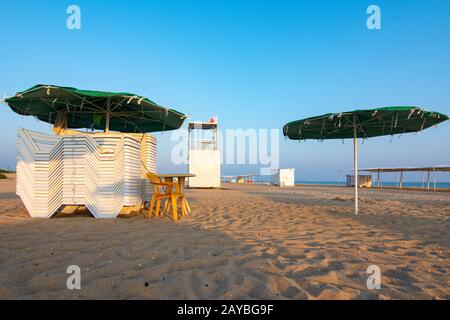 Gefaltete Liegestühle und eine leere Rettungsschwimmer Post an einem einsamen Sandstrand bei Sonnenuntergang Stockfoto