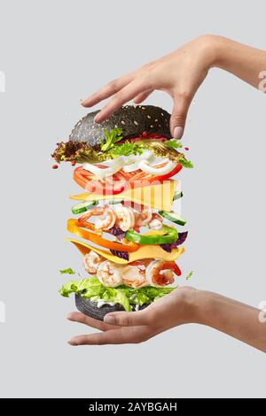 Fliegender Burger mit frischen Zutaten zwischen den Händen der Frau auf hellem Hintergrund. Stockfoto