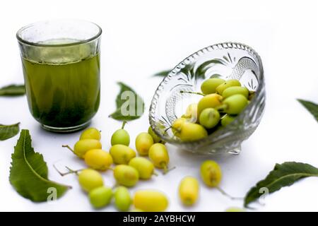 Entgiftung oder Entgiftung von Niemfrüchten in einem Glas, das auf Weiß isoliert ist, zusammen mit einigen Niemfrüchten oder Nimbodi oder Nimbudi in einer Glasschale. Stockfoto