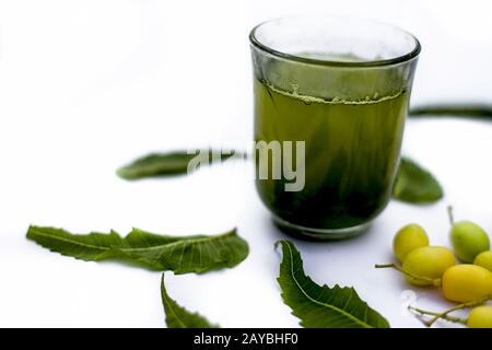 Entgiftung oder Entgiftung von Niemfrüchten in einem Glas, das auf Weiß isoliert ist, zusammen mit einigen Niemfrüchten oder Nimbodi oder Nimbudi in einer Glasschale. Stockfoto