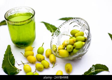 Entgiftung oder Entgiftung von Niemfrüchten in einem Glas, das auf Weiß isoliert ist, zusammen mit einigen Niemfrüchten oder Nimbodi oder Nimbudi in einer Glasschale.Horizontaler Schuss Stockfoto