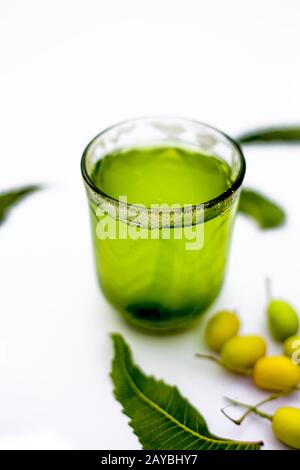 Entgiftung oder Entgiftung von Niemfrüchten in einem Glas, das auf Weiß isoliert ist, zusammen mit einigen Niemfrüchten oder Nimbodi oder Nimbudi in einer Glasschale.Vertikaler Schuss. Stockfoto