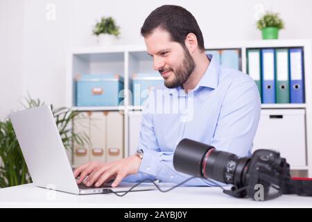 Bärtigen Fotograf in seinem Büro mit Laptop und Kamera. Stockfoto