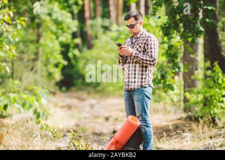 Hipster junger Mann mit Rucksack mit Smartphone auf wunderschönem Naturerlebnis.Reisekonzept. Reisen im Freien. Reisen und erkunden. Backpa Stockfoto