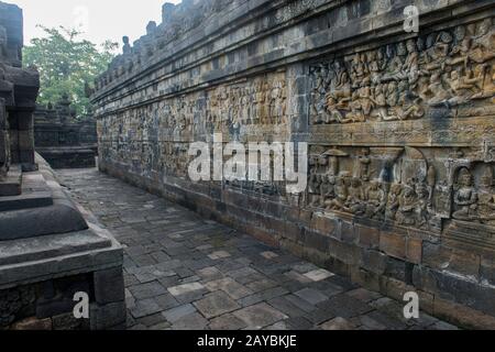 Steinbass-Reliefschnitzereien an einem schmalen Durchgang an einer unteren Plattform des Borobudur-Tempels (UNESCO-Weltkulturerbe, neuntes Jahrhundert), dem größten Budd Stockfoto