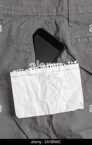 Schwarzes Smartphone-Gerät in der vorderen Tasche der formellen Arbeitshose in der Nähe eines weißen Notizbuchs. Modernes Gerät wird in den Menschen gelegt Stockfoto