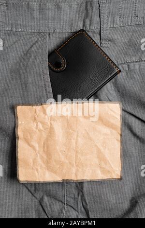 Kleine Tasche in der Hosentasche vorne neben dem braunen Notizblatt. Kleine Geldbörse wird in Mannhosen in der Nähe des Notationsbogens platziert. Stockfoto