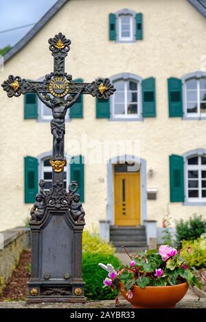 Kreuz- und Blumentopf im Hof eines Hauses im malerischen Dorf Monreal, Eifel, Deutschland Stockfoto