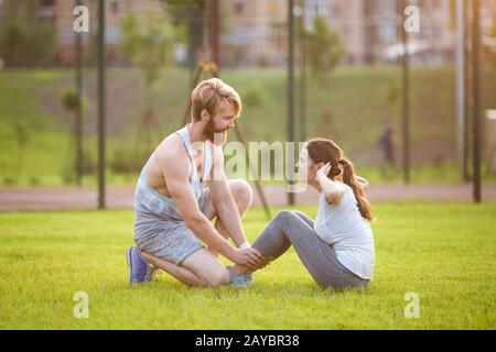 Sit ups Fitness-Paar, das trainiert, sitzt draußen im Gras. Passen Sie Leute, die Kreuztraining ausarbeiten. Frau, die Bauchkräschen macht Stockfoto