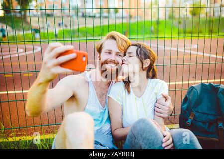 Ein Paar roter Haare und ein Bart eines europäischen Mannes und eine Frau ruhen, nachdem sie im Freien Sport gespielt haben. Der Kerl hält ein rotes Smartphone an Stockfoto