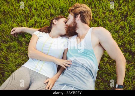 Thema ist Sport und ein gesunder Lebensstil. Auf dem grünen Gras, einem Rasen, ruht ein junges Mann- und Frauenpaar auf dem Rücken Stockfoto