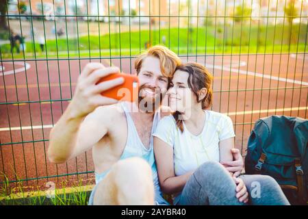 Ein Paar roter Haare und ein Bart eines europäischen Mannes und eine Frau ruhen, nachdem sie im Freien Sport gespielt haben. Der Kerl hält ein rotes Smartphone an Stockfoto