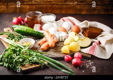 Prozess der Herstellung Okroshka Suppe. Häckseln, Rettich, Wurst und andere Zutaten auf Holz Schneidebrett Stockfoto