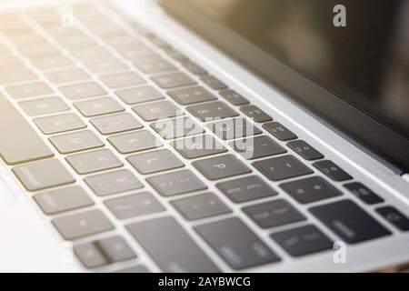 Nahaufnahme der selektiven Fokus-Laptop-Tastatur mit weißem Buchstaben auf schwarzer Taste und hellem Lichteffektiv von links oben. Stockfoto