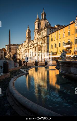 Blick vom Brunnen des Navona-Platzes von Netuno mit Schwerpunkt auf der Kirche der Heiligen Agnes und ihrer Reflexion an einem Sommermorgen. Stockfoto