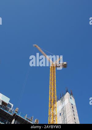 Blick auf einen hohen Turmkran, der auf großen Baustellen gegen einen blauen Himmel arbeitet Stockfoto