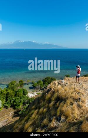 Ein Tourist auf dem Hügel auf Gili Kenawa, einer kleinen Insel der Küste von Sumbawa, Indonesien, Lombok Island mit dem aktiven Vulkan Mount Rinjani oder Stockfoto