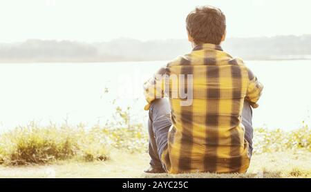 Ein einsamer Mann, der an sonnigen Tagen vor dem See sitzt - Konzept der Einsamkeit, des Aufbruchs, des Alleinstehenden. Stockfoto