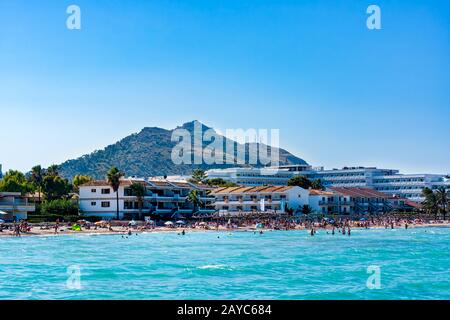 Touristen, die an einem Strand von Alcudia, türkisfarbenem Meer, einem sandigen Strand und Bergen, Mallorca, sonnige Ferien genießen Stockfoto