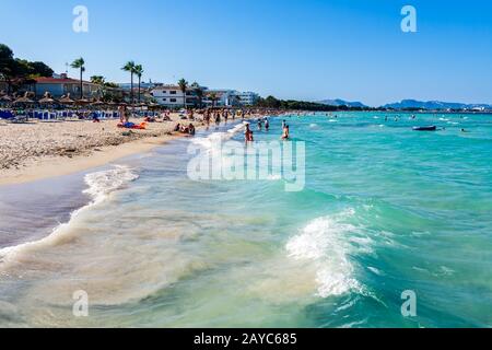 Touristen, die an einem Strand von Alcudia, türkisfarbenem Meer und einem sandigen Strand auf Mallorca Urlaub genießen Stockfoto