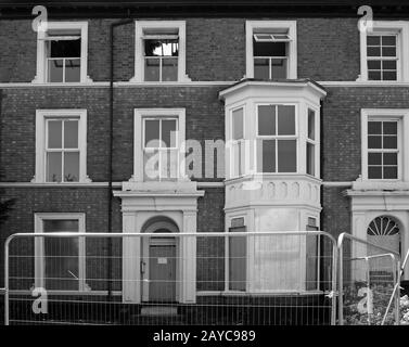 Monochromes Bild einer Reihe verfallener verfallener verderbter Häuser in einer Straße hinter einem Metallzaun in southport merseyside Stockfoto