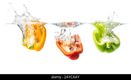 Rote, gelbe und grüne Paprikahälften spritzen in Wasser Stockfoto