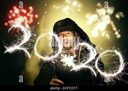 Mann feiert Silvester mit Feuerwerk und schreibt die Zahlen 2020 mit einem Glitzer während einer langen Belichtungsfotograf Stockfoto