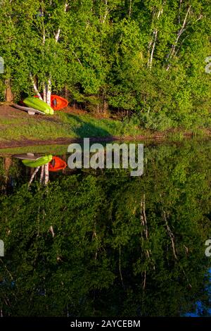 Boote und Bäume, die über das ruhige Wasser des Lac Mercier im Old Mont-Tremblant Village in den Laurentians in der Provinz Quebec, Kanada, reflektieren. Stockfoto