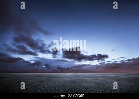 Leerer Asphaltboden mit dramatischem Himmel bei Sonnenuntergang. Stockfoto