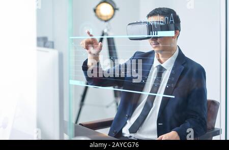 Asiatische Geschäftsleute, die eine virtuelle Reality-Brille tragen und die Wachstumskarte eines Unternehmens in einem Büro zeigen. Stockfoto