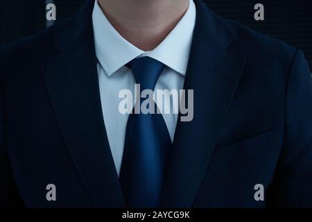 Ein Teil der Körperseite des Menschen faltete seine Arme in schwarzem Anzug auf schwarzem Grund Stockfoto